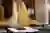 Person in mustard yellow blazer using calculator while working on laptop with documents on desk.