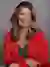 Headshot of Suzy Martinek, wearing a red blazer and necklace, posed against a gray brick wall background.